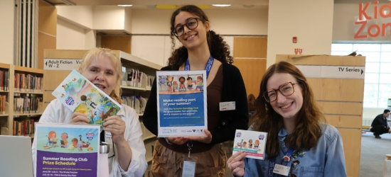 Three library staff members smiling and holding Summer Reading Club posters